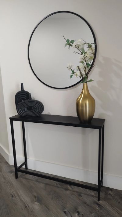 Round mirror over black console with gold vase